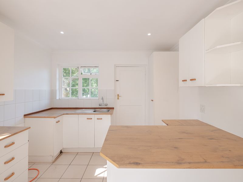 A bright, empty kitchen featuring white cabinetry, wood-look laminate countertops, tiled flooring, and a functional sink area with natural light.