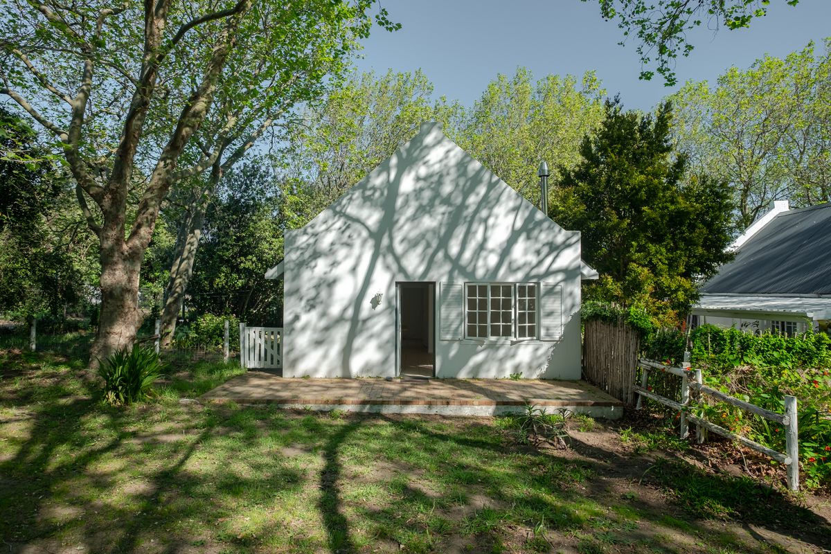 A charming cottage-style rear elevation featuring a white facade, brick patio, and mature garden surroundings.