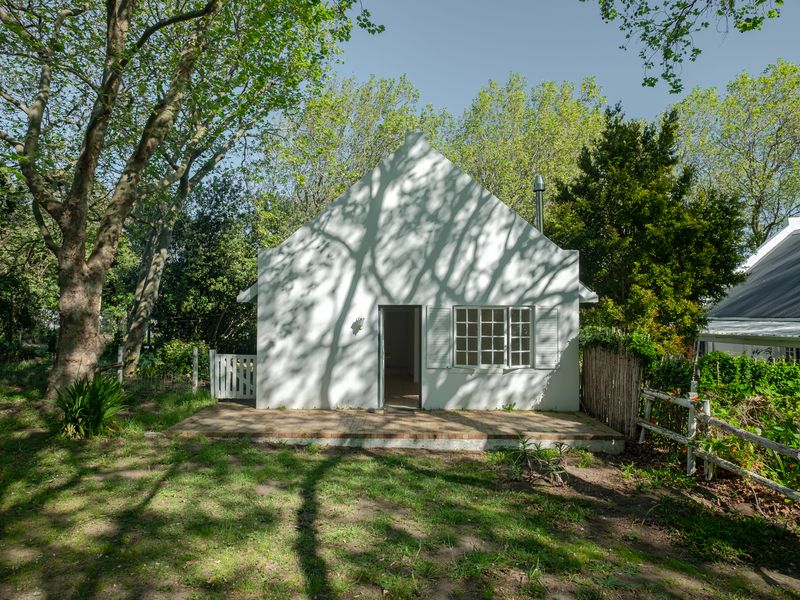 A charming cottage-style rear elevation featuring a white facade, brick patio, and mature garden surroundings.