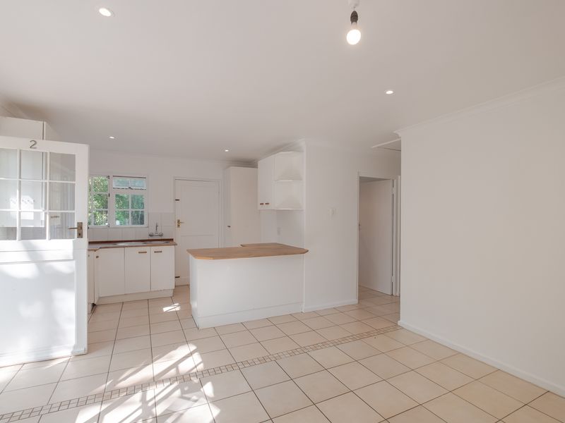 An open-plan kitchen and living area featuring tiled flooring, white cabinetry, a breakfast counter, and a classic stable door leading outdoors.
