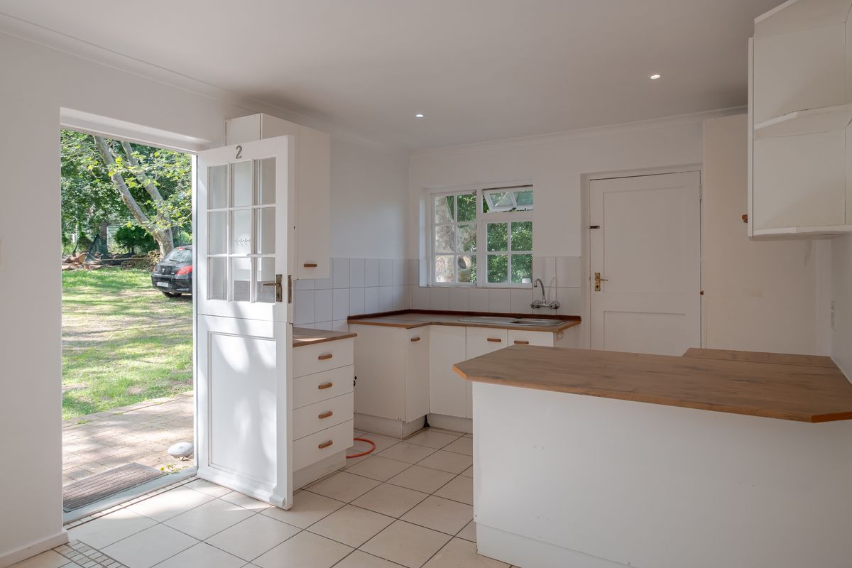 A bright, empty kitchen featuring white cabinetry, laminate countertops, tiled flooring, and a stable door providing direct access to the garden.