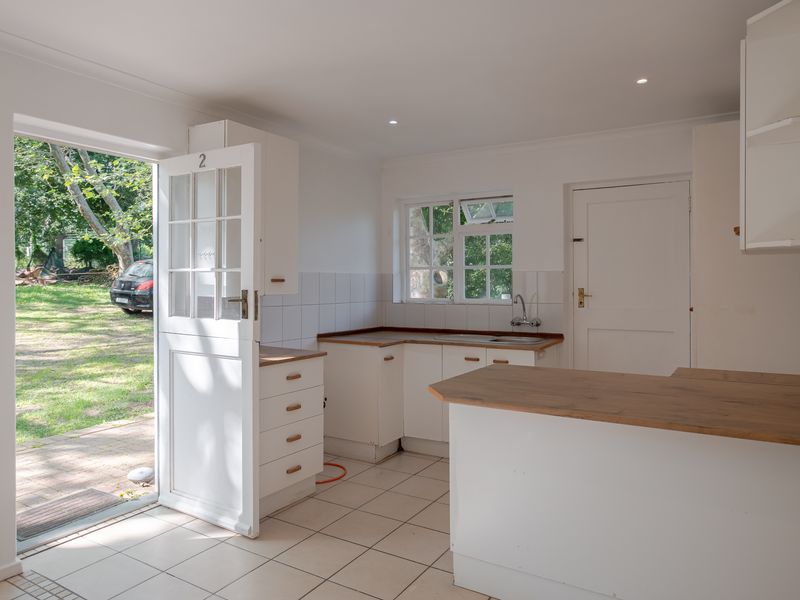 A bright, empty kitchen featuring white cabinetry, laminate countertops, tiled flooring, and a stable door providing direct access to the garden.