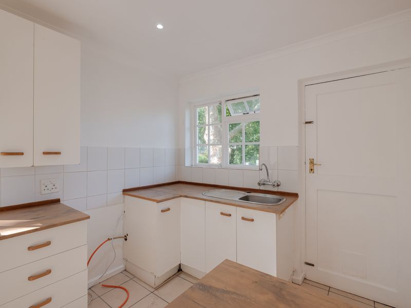 A functional scullery or laundry area featuring white cabinetry, wood-look laminate countertops, a stainless steel sink, and tiled flooring.