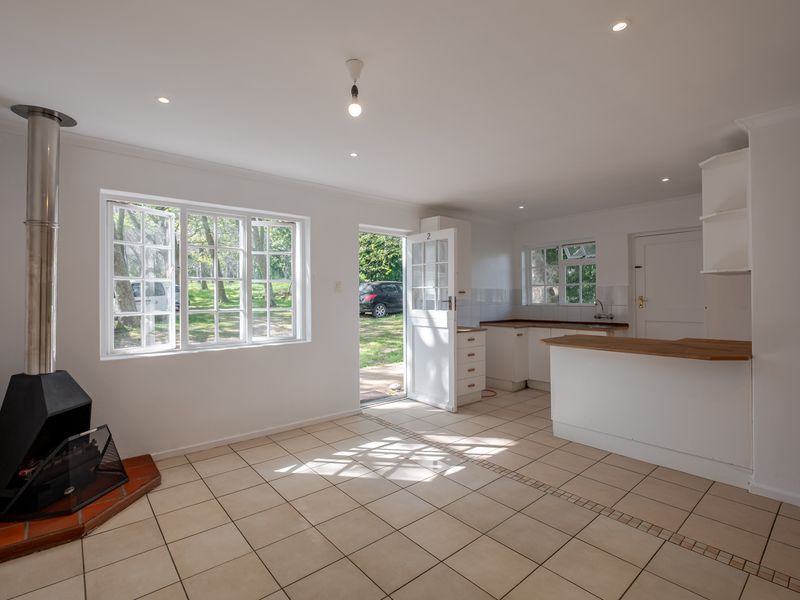 Bright open-plan living and kitchen area featuring tiled floors, a modern freestanding fireplace, and direct access to the garden through a glass-paneled door.