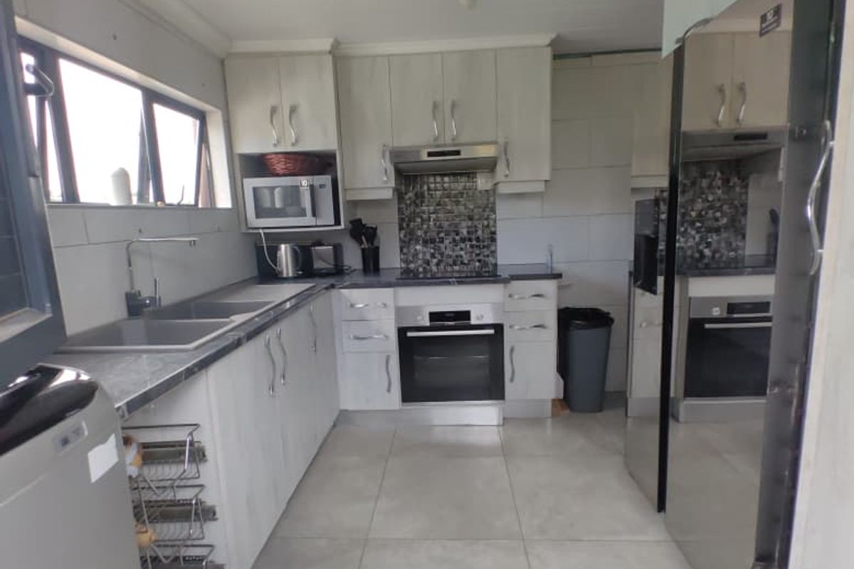 A functional kitchen featuring light-toned cabinetry, tiled splashbacks, built-in oven, extractor fan, and large floor tiles.
