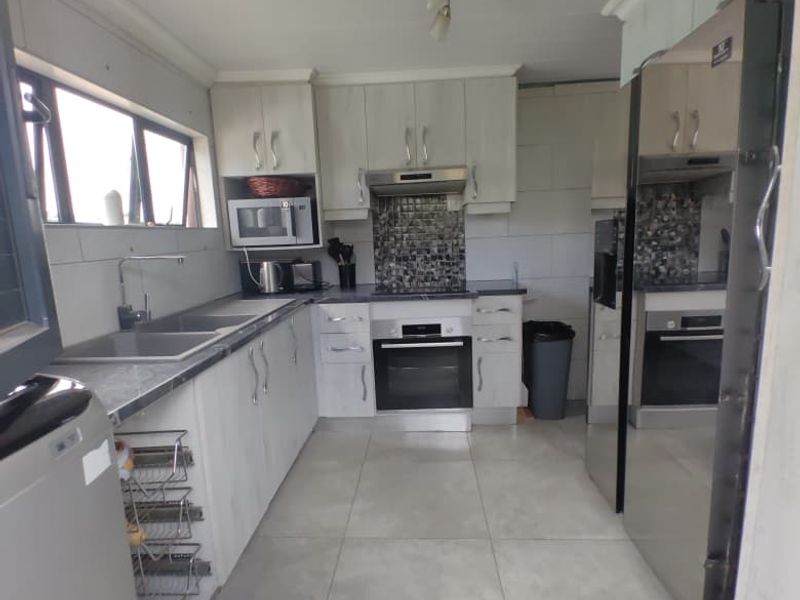 A functional kitchen featuring light-toned cabinetry, tiled splashbacks, built-in oven, extractor fan, and large floor tiles.