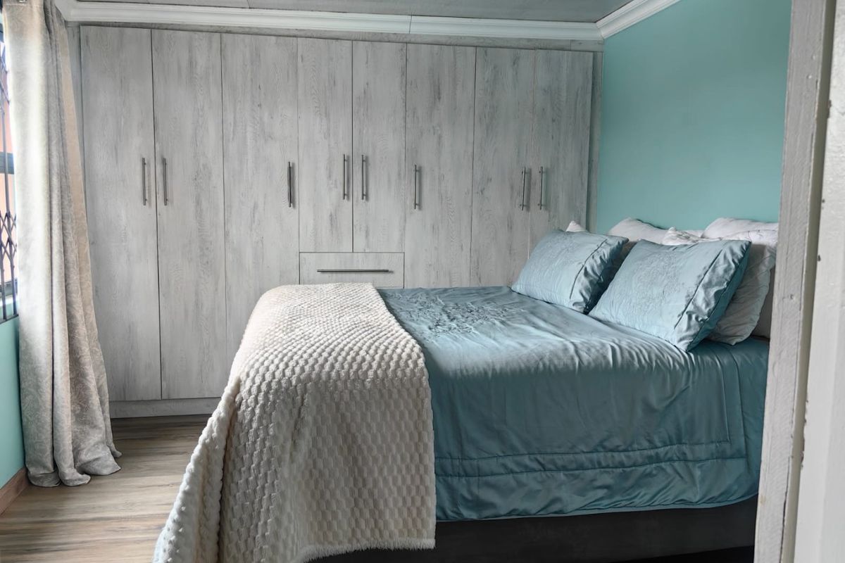 A well-maintained bedroom featuring extensive built-in cupboards with a wood-grain finish, laminate flooring, and decorative ceiling cornicing.