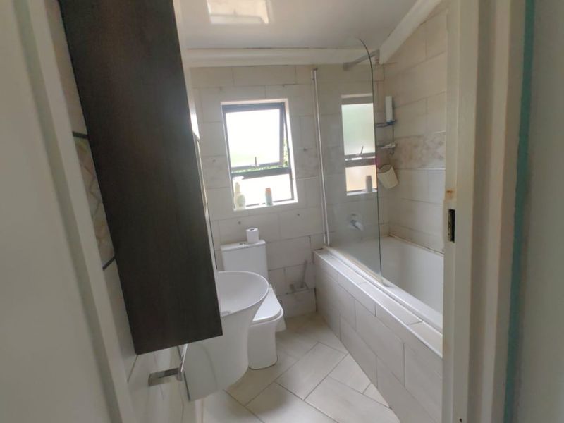 A functional bathroom featuring a bathtub with a glass shower screen, toilet, and neutral wall and floor tiling.