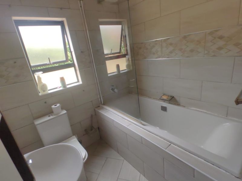 A functional bathroom featuring a bathtub with a glass screen, pedestal basin, toilet, and neutral tiled finishes throughout.