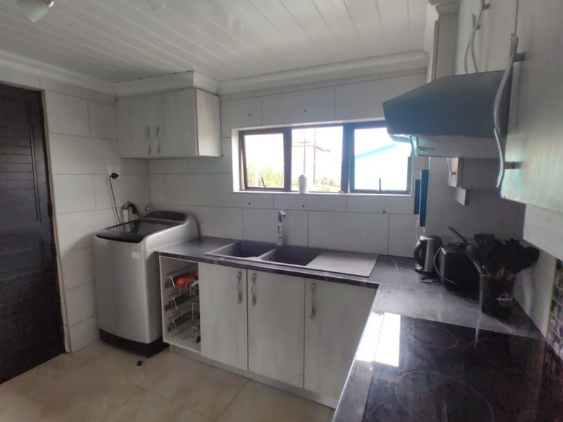 Functional kitchen featuring built-in cabinetry, a double sink, electric hob with extractor fan, and tiled finishes throughout.