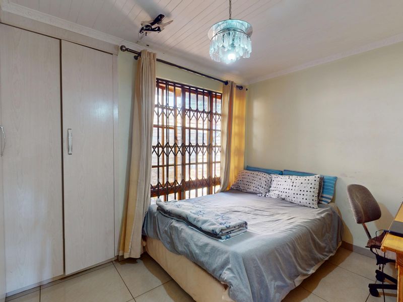 A functional bedroom featuring built-in wardrobes, tiled flooring, and a security gate on the window, offering a practical and secure living space.