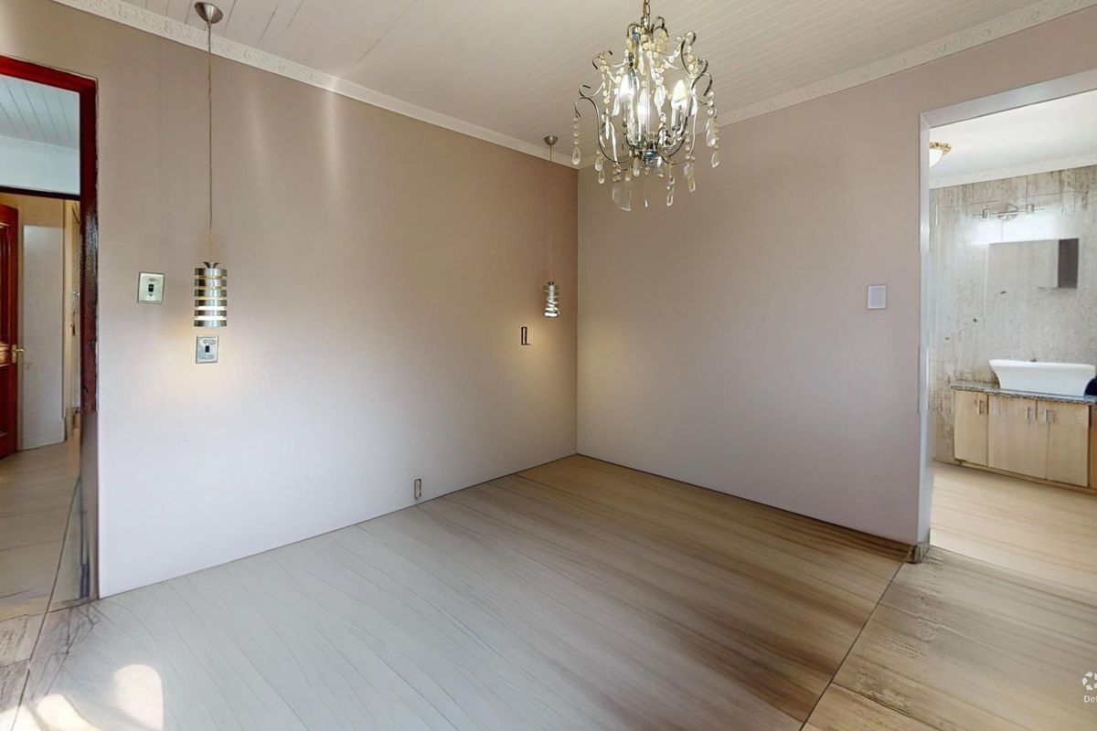 An empty living area featuring timber-look flooring, a timber-panelled ceiling with decorative cornicing, and multiple light fixtures, with an adjacent bathroom visible.