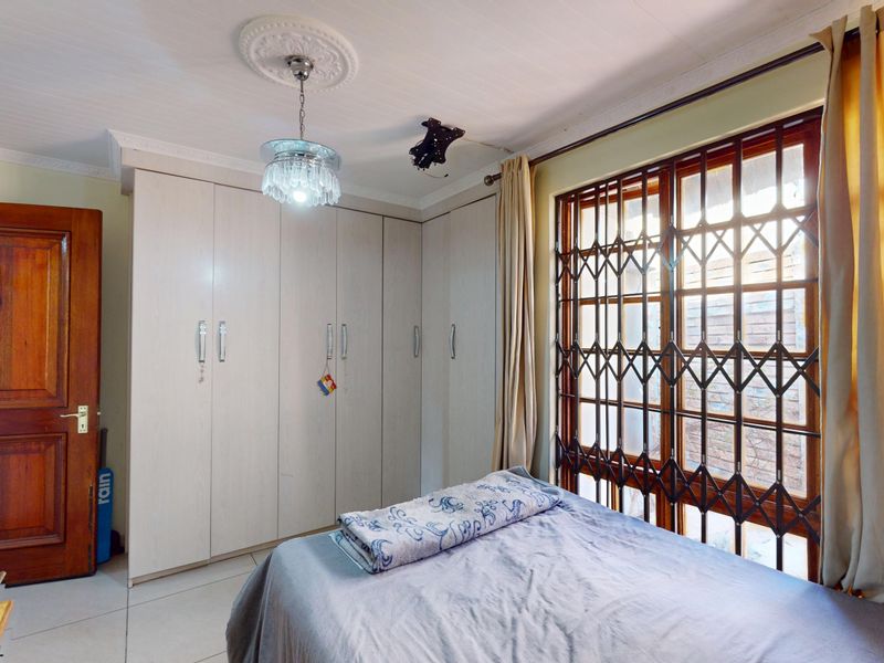 A bedroom featuring built-in cupboards, tiled flooring, and a security gate on the window, providing functional storage and basic security.