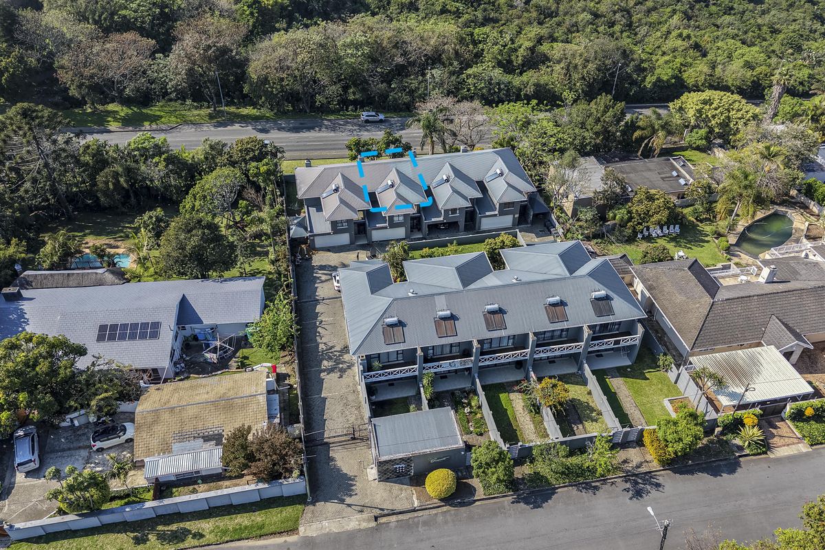 Aerial view of a townhouse complex featuring metal roofing, solar water heating systems, and paved driveway access within a landscaped residential setting.