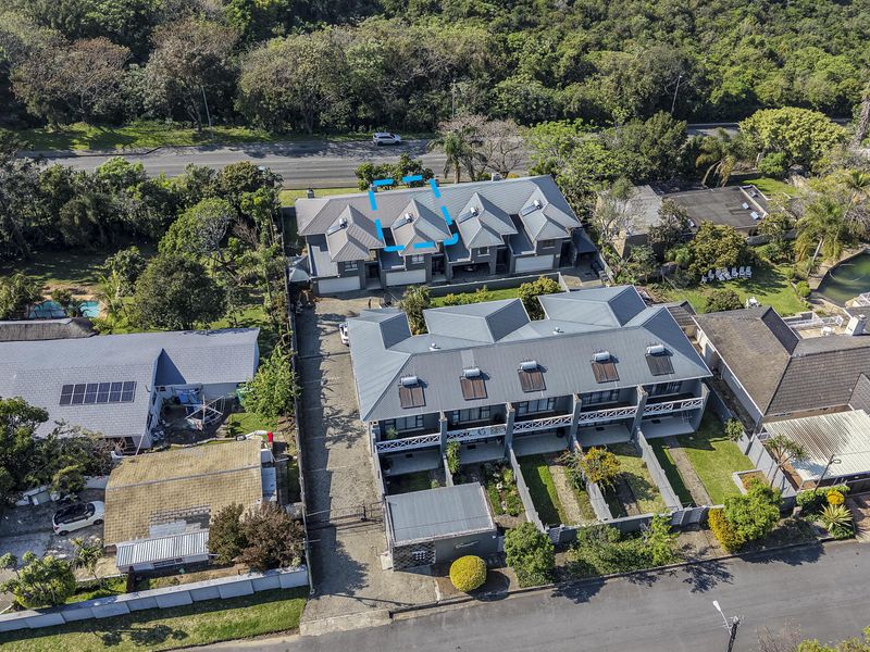 Aerial view of a townhouse complex featuring metal roofing, solar water heating systems, and paved driveway access within a landscaped residential setting.
