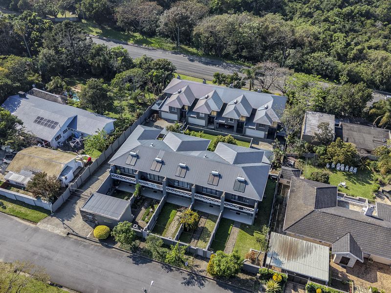 Aerial view of a townhouse complex featuring metal roofing, solar geysers, private garden courtyards, and paved driveway access.