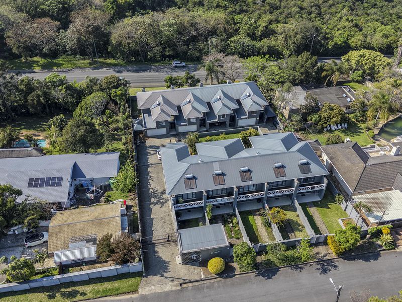 Aerial view of a townhouse complex featuring metal roofs, solar water heating systems, private garden plots, and a shared paved driveway.