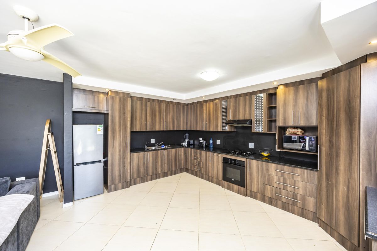 Modern kitchen featuring dark wood cabinetry, granite-look countertops, built-in oven, gas hob, and tiled flooring in an open-plan layout.