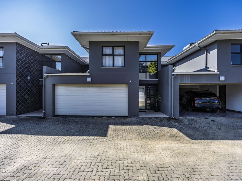 Modern townhouse exterior featuring a paved driveway, double garage, and integrated carport with contemporary grey facade finishes.