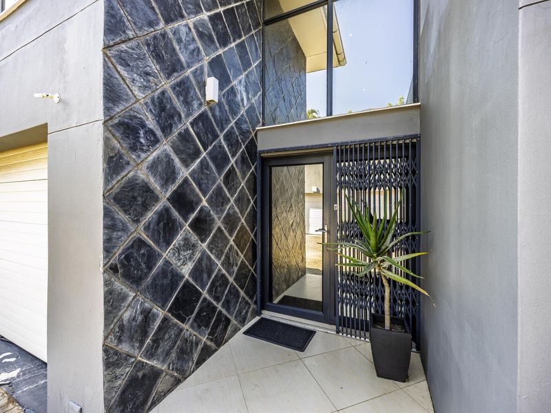 Modern townhouse entrance featuring a striking diamond-patterned stone feature wall, secure metal gate, and glass door access.