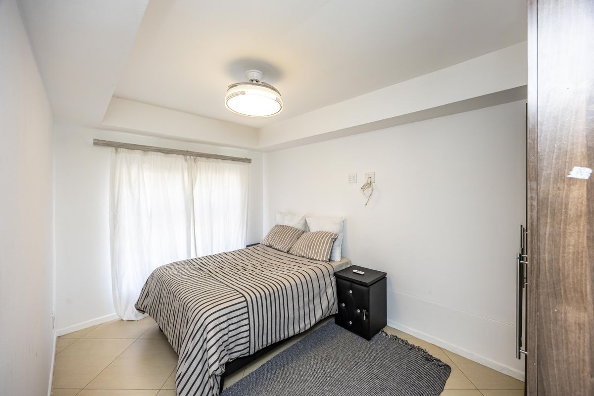 A well-maintained bedroom featuring tiled flooring, a central ceiling light fixture, and a built-in wardrobe.