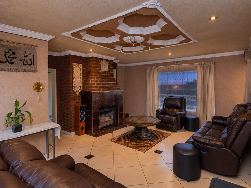 Spacious living room featuring a prominent brick fireplace, decorative ceiling detailing, and neutral tiled flooring, creating a warm and inviting atmosphere.