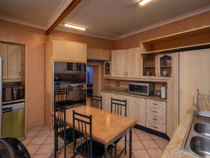 A functional kitchen featuring light wood cabinetry, tiled splashbacks, laminate countertops, and a double bowl stainless steel sink with integrated dining space.