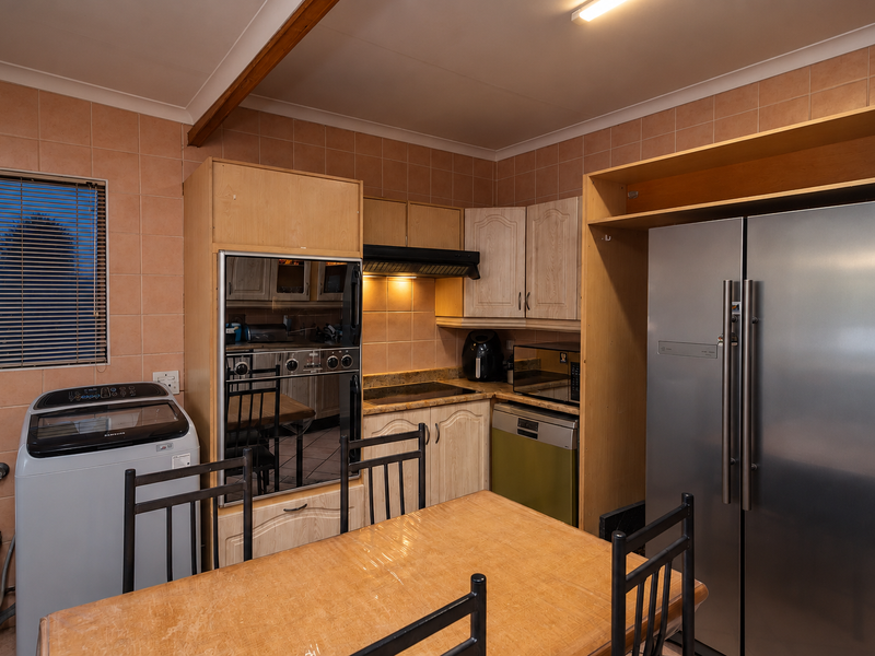 Functional kitchen featuring built-in oven, hob, extractor fan, and integrated dishwasher with tiled splashbacks and ample cabinetry.