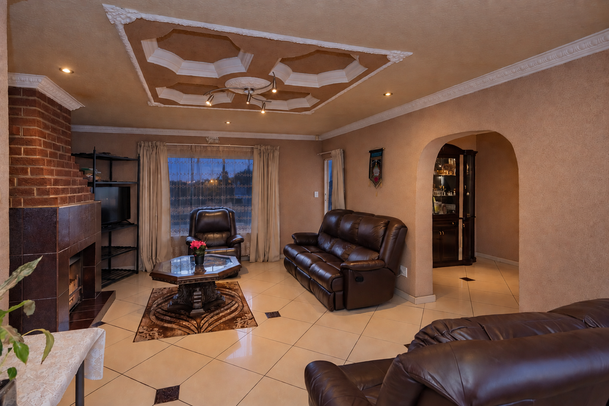 Spacious living room featuring a brick fireplace, decorative ceiling detailing, tiled flooring, and an arched entryway leading to adjacent living spaces.