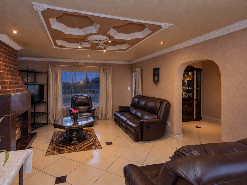 Spacious living room featuring a brick fireplace, decorative ceiling detailing, tiled flooring, and an arched entryway leading to adjacent living spaces.