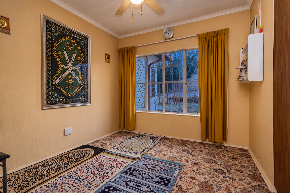 A bedroom featuring patterned carpeting, a ceiling fan, and a window fitted with security bars, offering a functional and lived-in space.