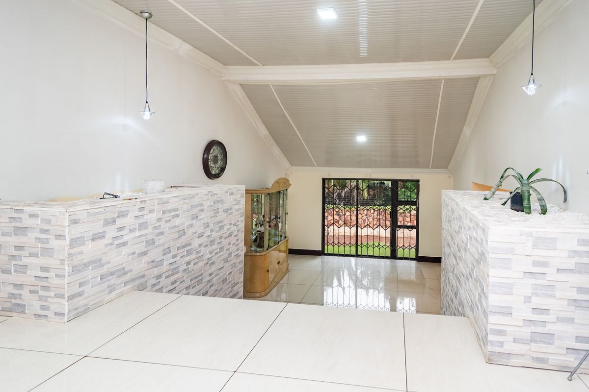 Spacious living area featuring vaulted ceilings, modern stone-clad feature walls, tiled flooring, and a secure rear entrance leading to the garden.