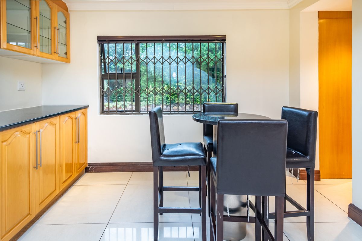A functional kitchen area featuring wooden cabinetry, black granite countertops, and tiled flooring, with a window fitted with security bars.