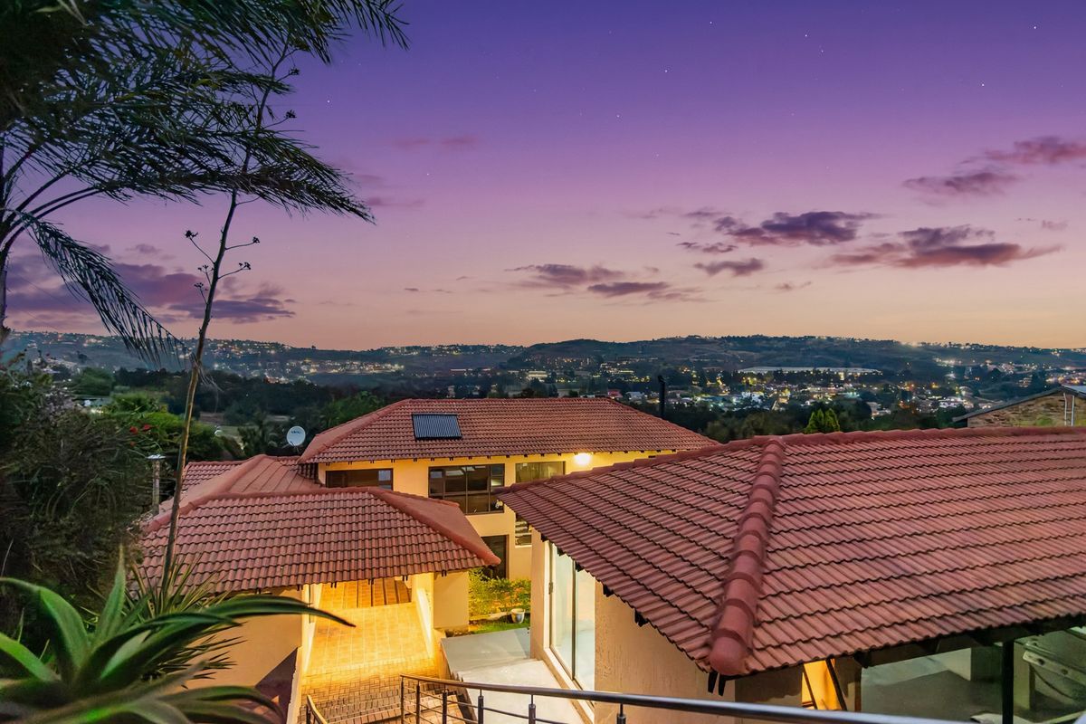 An elevated aerial view of the property at dusk, showcasing the tiled roof structure, solar water heating system, and surrounding landscape.