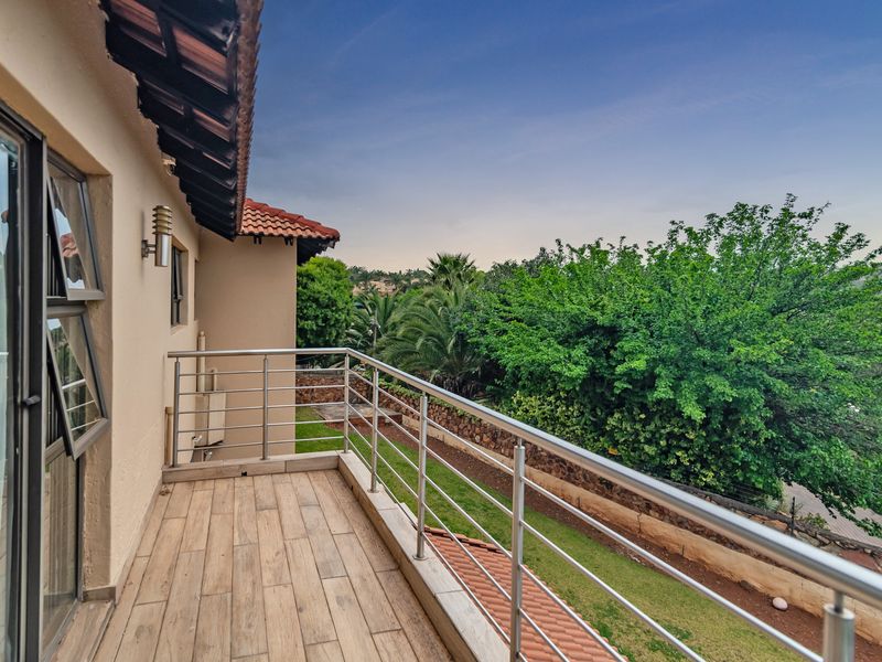 A well-maintained balcony featuring wood-look tiled flooring and a modern stainless steel balustrade, offering a pleasant view of the garden and surrounding greenery.