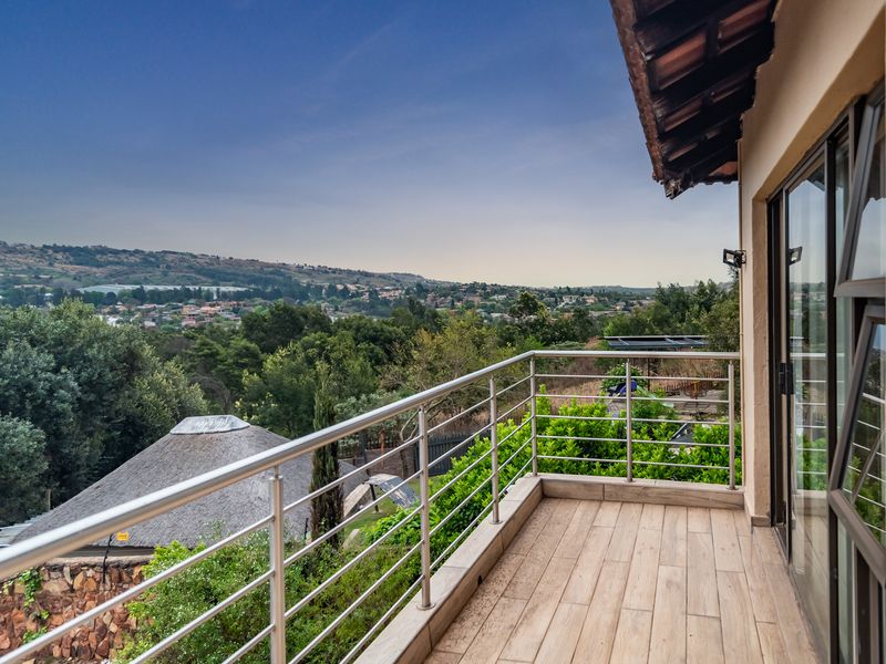 A spacious balcony featuring a modern stainless steel balustrade, wood-look tiled flooring, and expansive elevated views of the surrounding landscape.