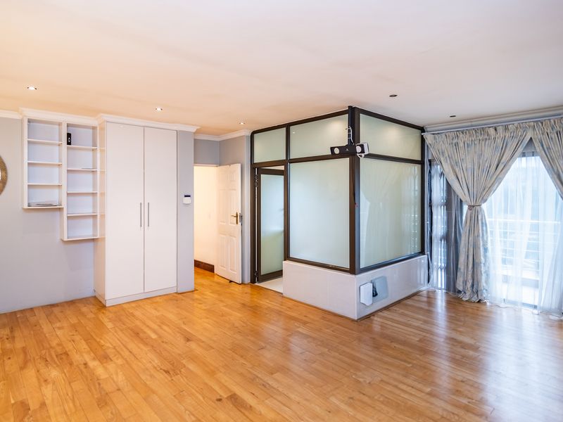 Spacious bedroom featuring hardwood flooring, built-in cupboards with integrated shelving, and a modern frosted glass partition creating a distinct internal zone.