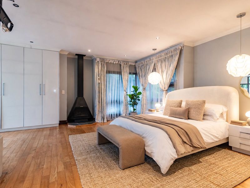 A well-appointed bedroom featuring hardwood flooring, a modern freestanding fireplace, built-in wardrobes, and elegant recessed lighting.