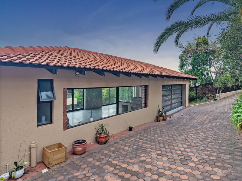 Front exterior view of the property featuring a terracotta tiled roof, paved driveway, and large windows providing a glimpse into the interior space.