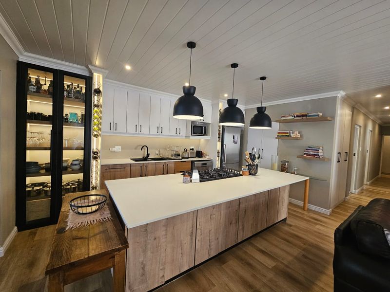 Modern kitchen featuring a large island with gas cooktop, sleek cabinetry, integrated appliances, and stylish pendant lighting, finished with high-quality timber-look flooring.
