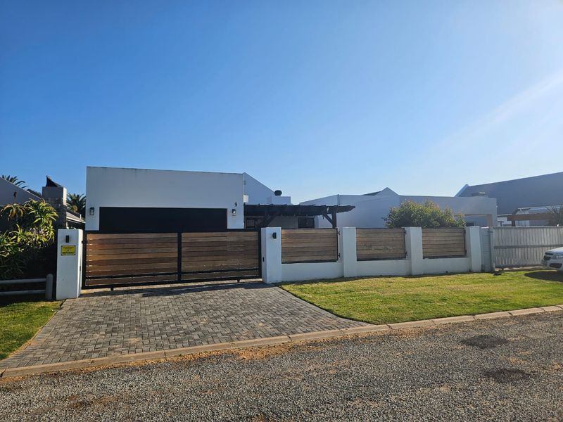 Front elevation of a modern house featuring a paved driveway, timber slat boundary wall, secure gate, and a pergola over the entrance area.