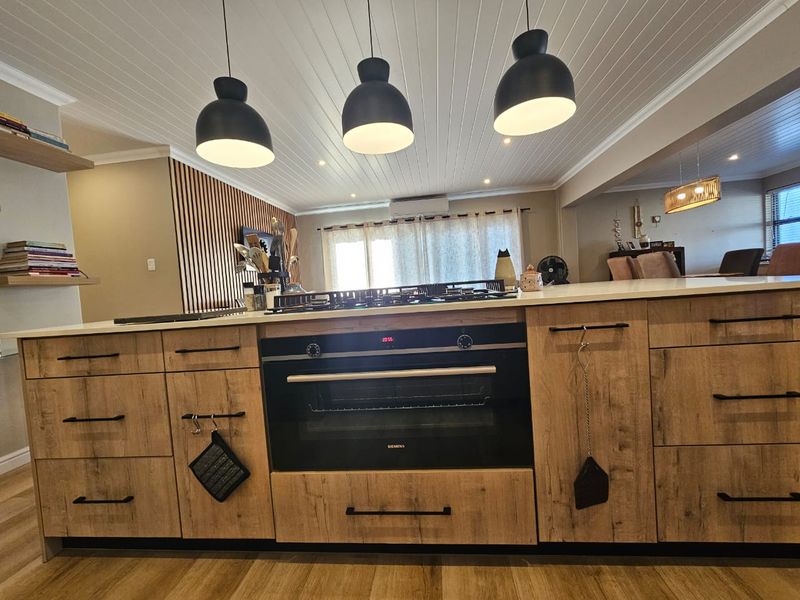 Modern kitchen featuring a large island with built-in oven and gas cooktop, complemented by timber-look cabinetry and stylish slatted wall detailing.