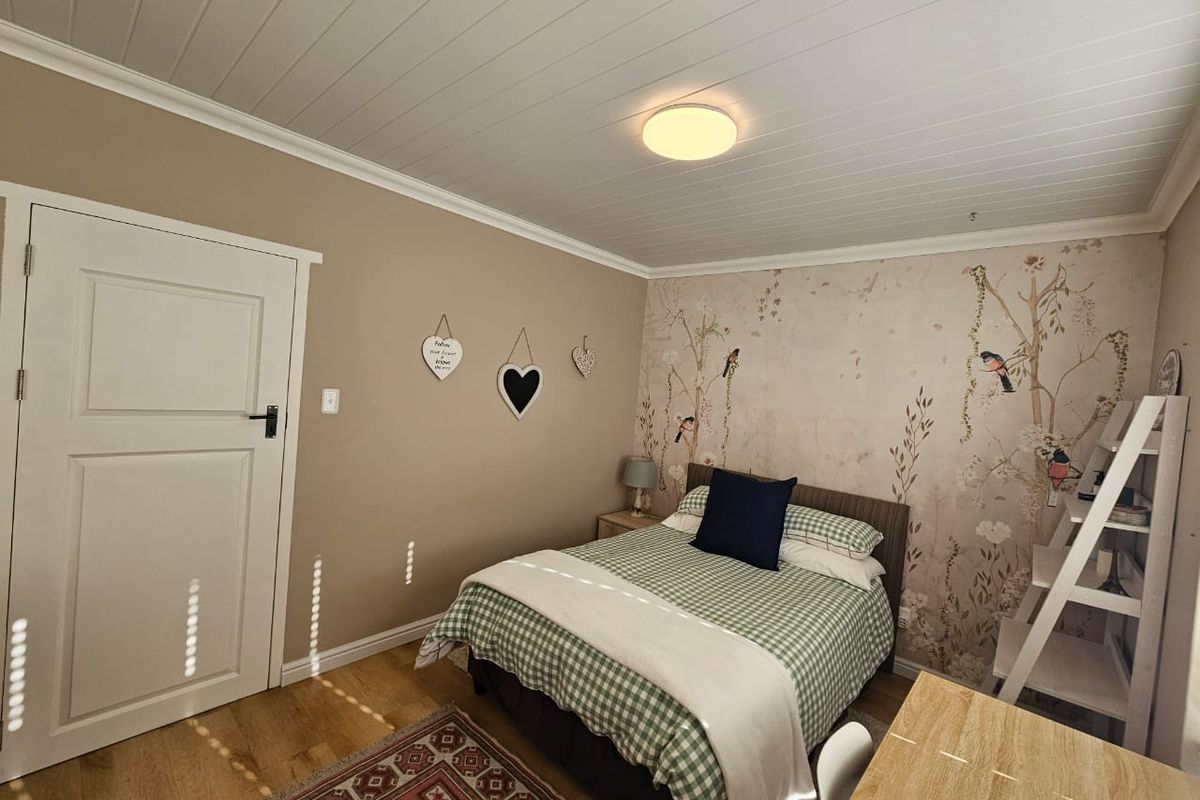 A well-maintained bedroom featuring a tongue and groove ceiling, laminate flooring, and a decorative feature wallpaper wall.