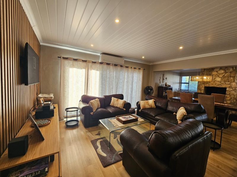Spacious open-plan living and dining area featuring a modern timber slat feature wall, stone fireplace surround, and recessed ceiling lighting.