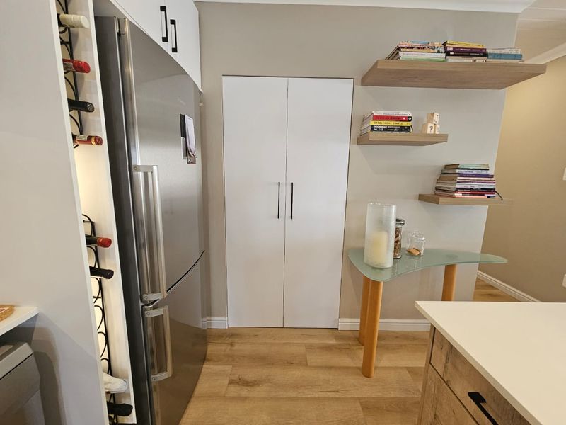 A modern kitchen area featuring a built-in wine rack, sleek pantry cabinetry, and floating wooden shelves, complemented by light wood-look laminate flooring.