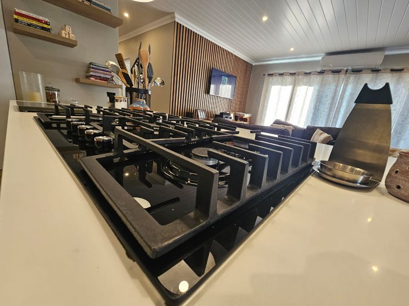 Modern open-plan living area featuring a sleek gas cooktop on a stone island, timber slat feature wall, and contemporary tongue and groove ceiling.