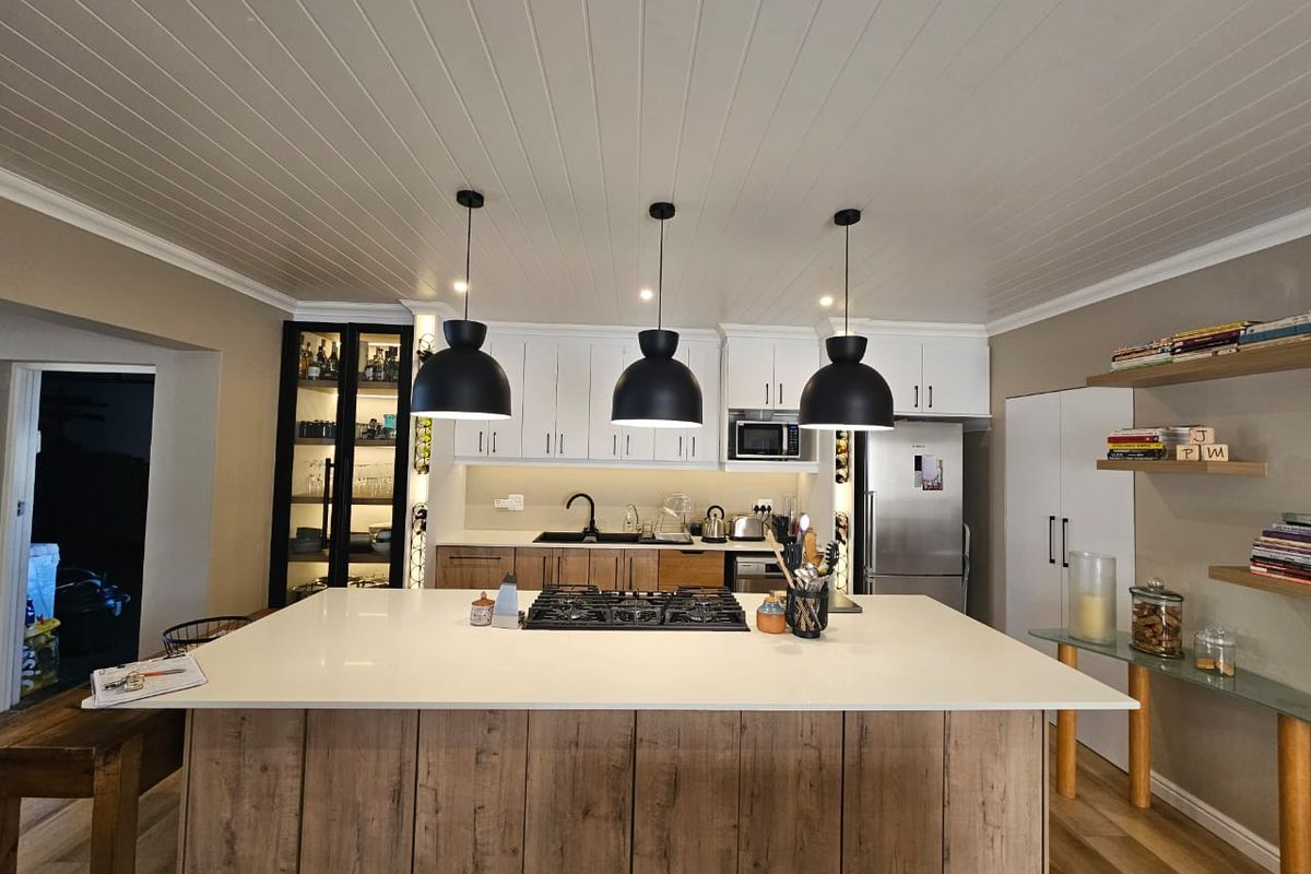 Modern kitchen featuring a large central island with gas cooktop, stone countertops, ample cabinetry, and stylish pendant lighting under a tongue and groove ceiling.