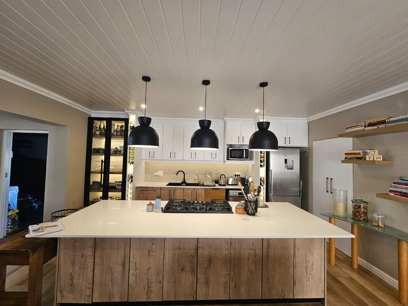 Modern kitchen featuring a large central island with gas cooktop, stone countertops, ample cabinetry, and stylish pendant lighting under a tongue and groove ceiling.