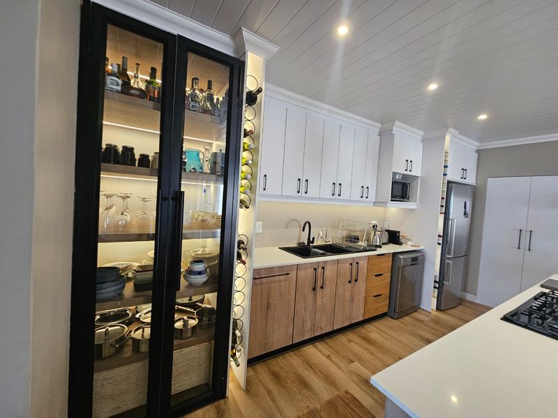 Modern kitchen featuring two-tone cabinetry, stone countertops, integrated appliances, a dedicated glass-front display cabinet, and stylish recessed lighting.
