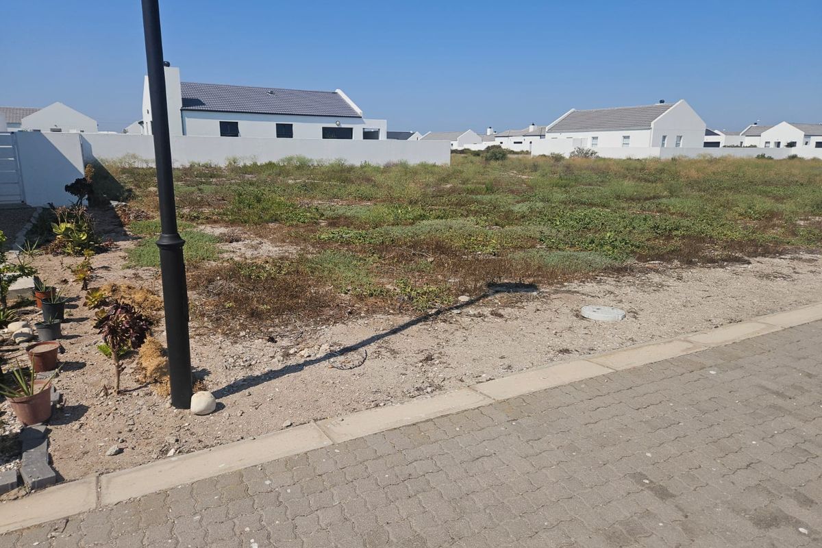 A vacant residential plot situated in a developed estate, featuring level ground and street-side access.